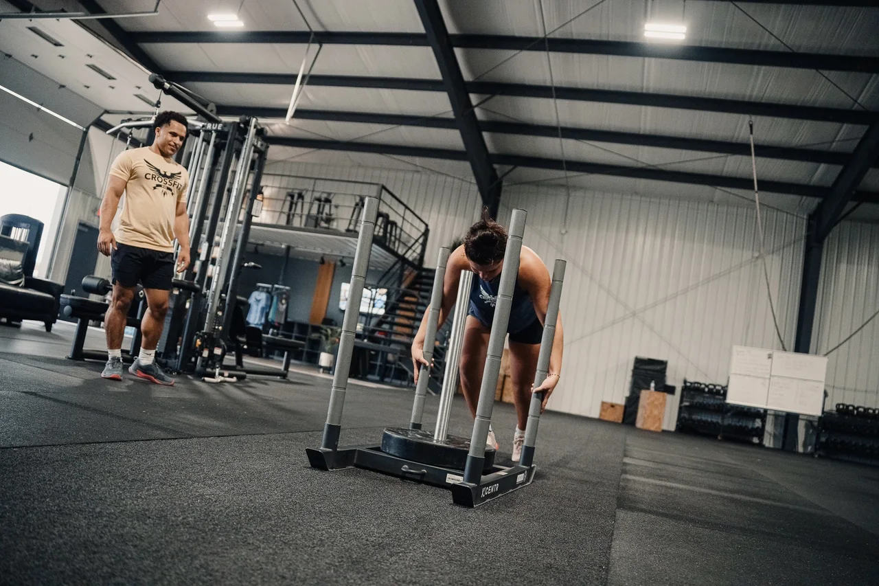 Coach watching an athlete push a weighted sled across the gym floor at CrossFit Fig.