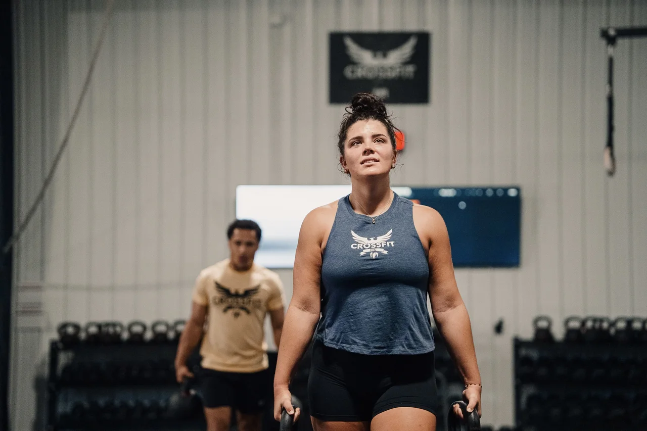 Athlete carrying a kettlebell in each hand with another athlete behind her at CrossFit Fig.